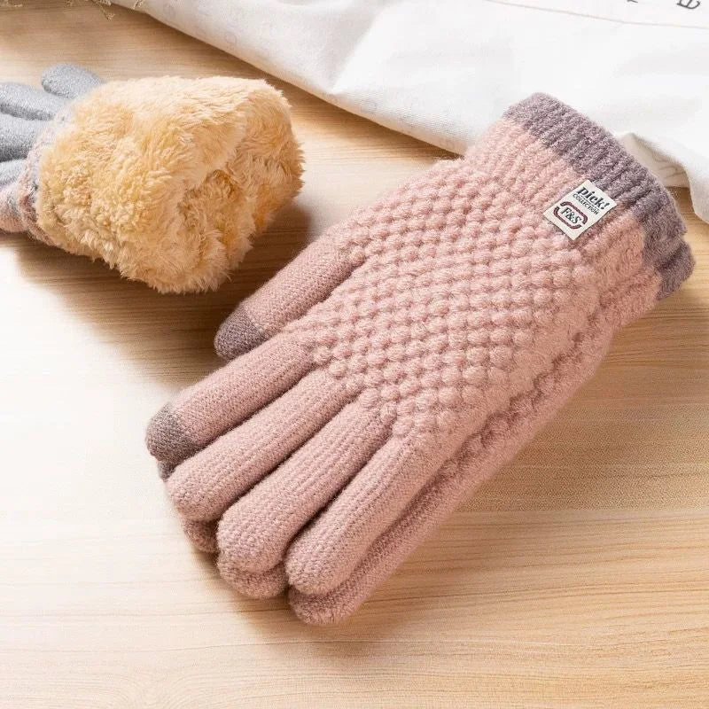 A pair of light pink knitted thermal gloves with gray accents resting on a wooden surface.