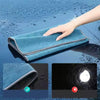A hand is holding a blue microfiber car cleaning towel on a wet surface, showing the texture and absorbency.