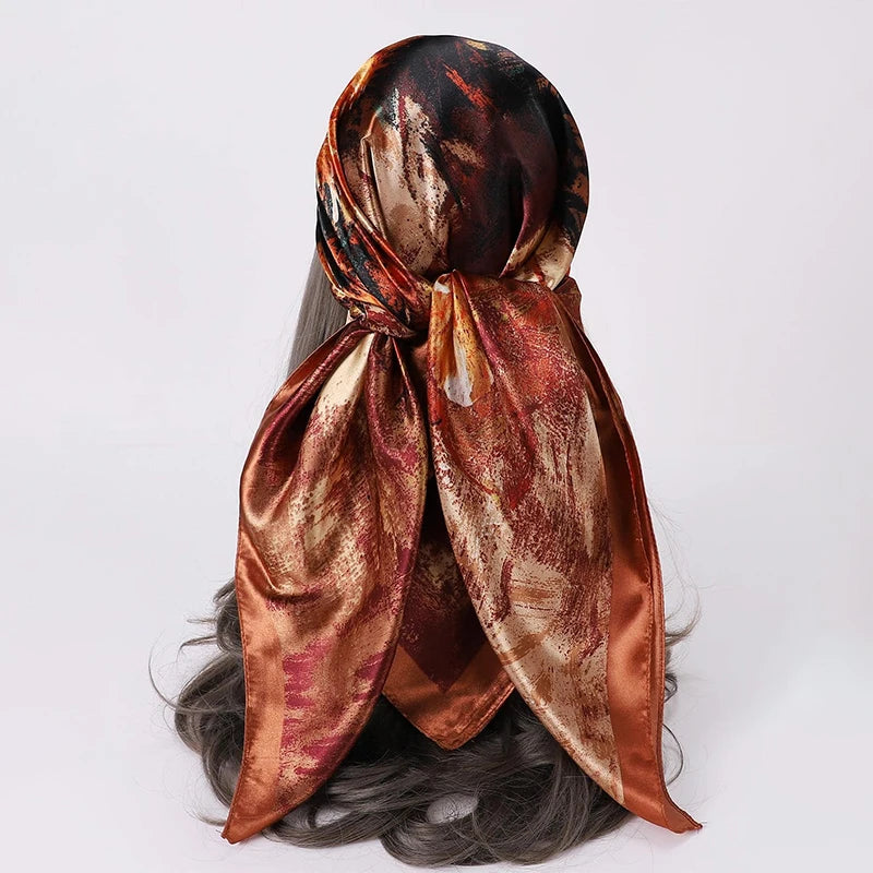 A draped, shiny satin scarf in shades of copper and rose gold is shown tied around a person's hair.