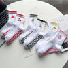 Un ensemble de chaussettes de yoga blanches avec broderies rouges et vertes et antidérapantes, présentées sur une surface bla