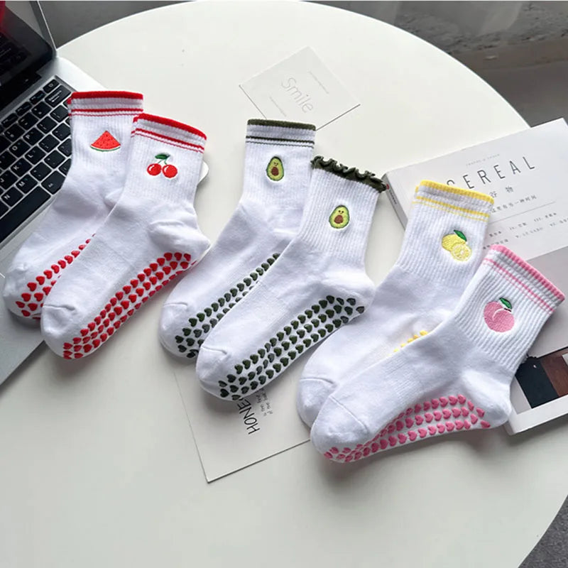 Un ensemble de chaussettes de yoga blanches avec broderies rouges et vertes et antidérapantes, présentées sur une surface bla