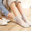 A person's hands are placing lace mesh ankle socks onto a wooden floor next to a pair of beige women's shoes.