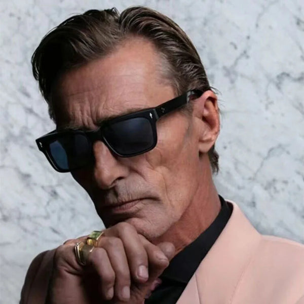 Gros plan d'un homme portant des lunettes de soleil Rivet Anti-Light noires sur un fond marbré gris clair.