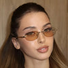 Close-up of a woman wearing rimless oval gradient sunglasses with gold accents.