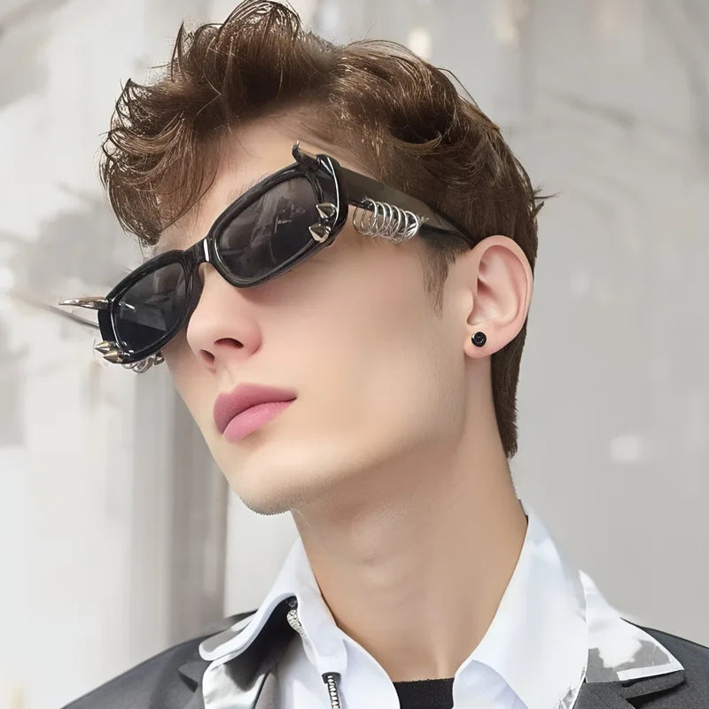 A close-up of a male model wearing black spiked rivet sunglasses and a white collared shirt.
