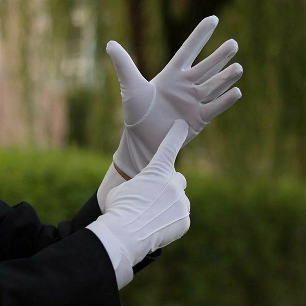 Una mano con un guante de algodón blanco en primer plano contra un fondo verde y desenfocado al aire libre.