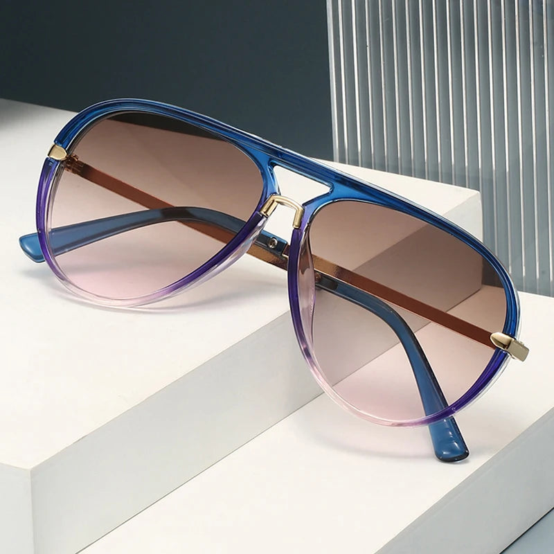 A pair of retro pilot sunglasses with gradient purple and pink lenses resting on a white surface.