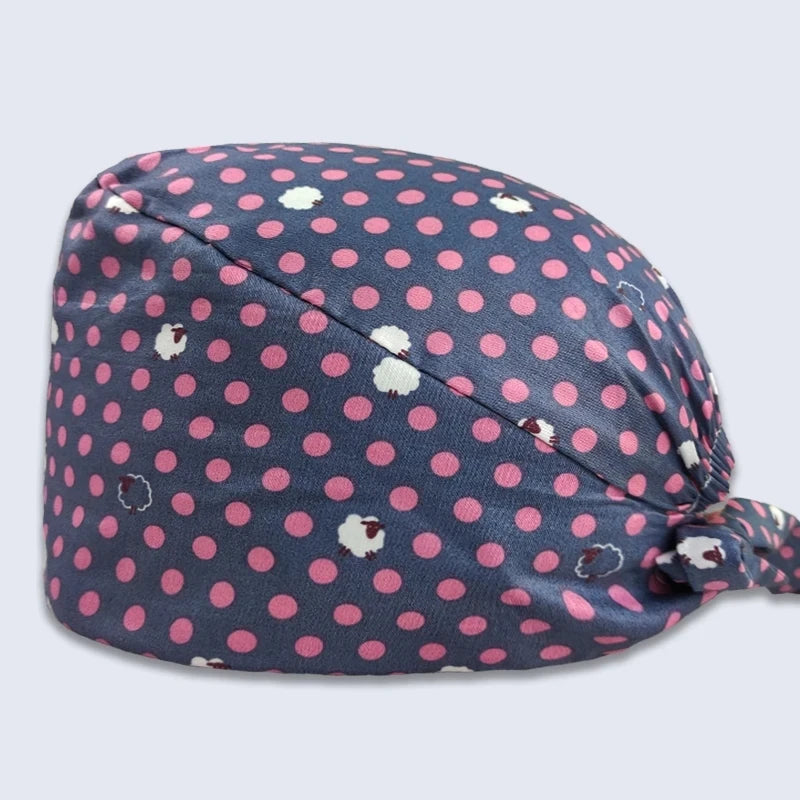 A navy blue cotton surgical cap with a pink polka dot pattern and white embroidered details.