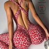 A woman wearing a red leopard print seamless yoga jumpsuit, posing in a studio setting.