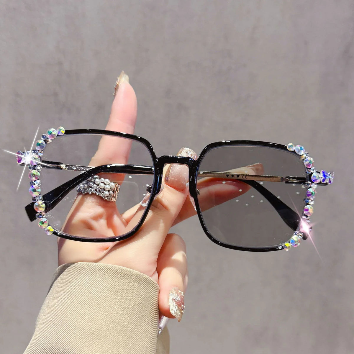 A hand holds a pair of black photochromic eyeglasses decorated with sparkling diamonds and rhinestones.