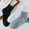 Eine Stapel von drei Herren-Atmungsaktiven Baumwoll-Knöchelsocken in Schwarz, Weiß und Grau neben einem Buch.