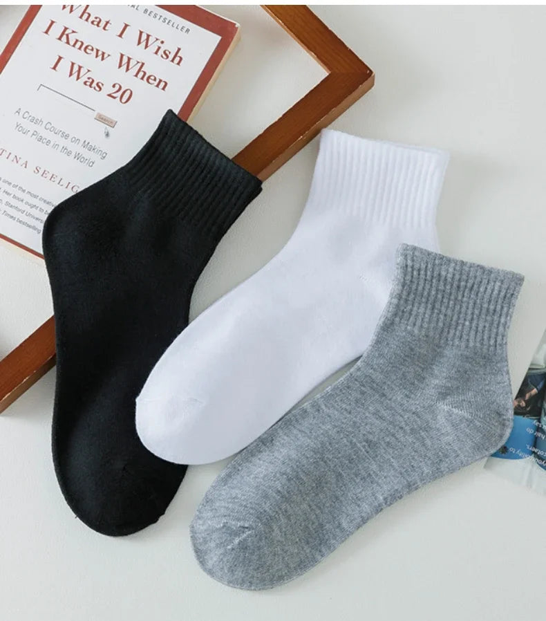 Eine Stapel von drei Herren-Atmungsaktiven Baumwoll-Knöchelsocken in Schwarz, Weiß und Grau neben einem Buch.