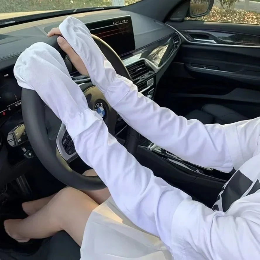 A person wearing white long-sleeved UV protection arm sleeves is gripping a steering wheel inside a car.