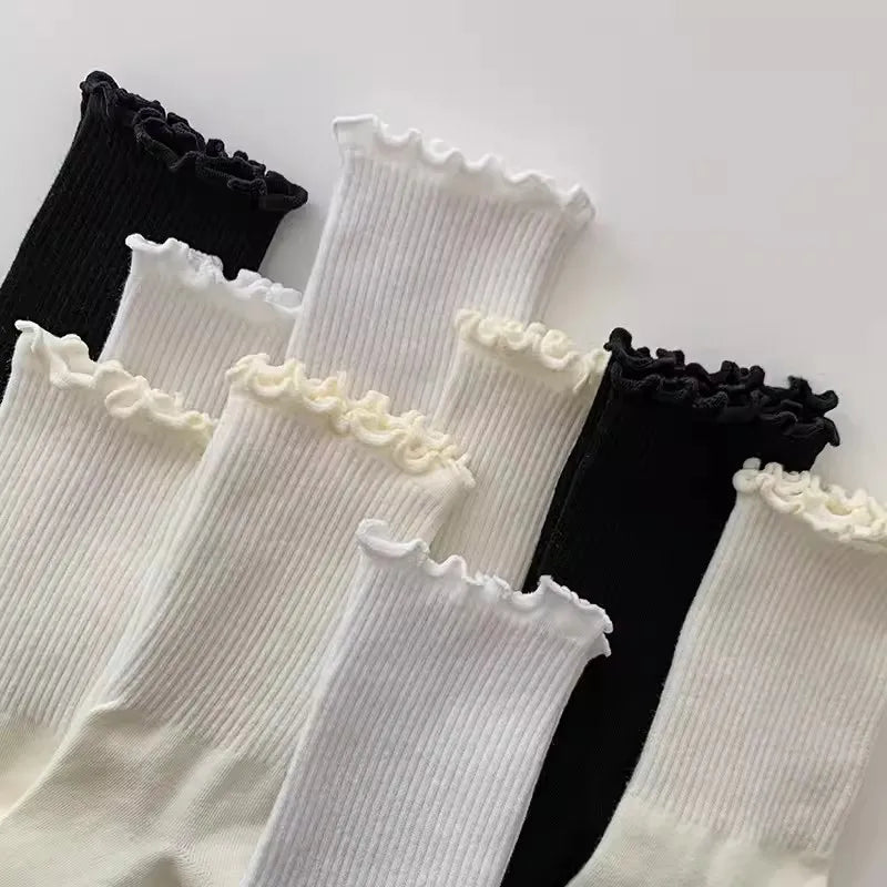 A stack of three cotton ruffle ankle socks in black and white are displayed on a white background.