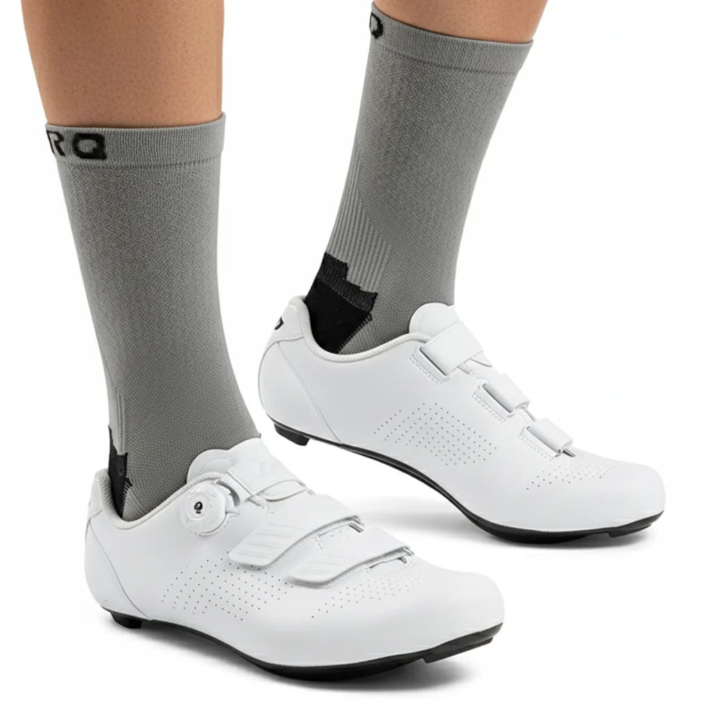 A pair of white cycling shoes and gray socks are shown on a person's foot.