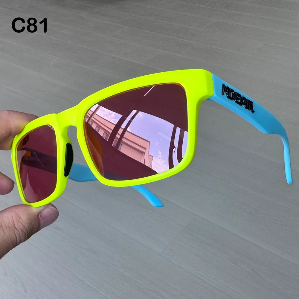 Ein Paar neongelbe Sonnenbrille mit blauen Rahmen wird in einer Hand vor einem hellgrauen Hintergrund gehalten.