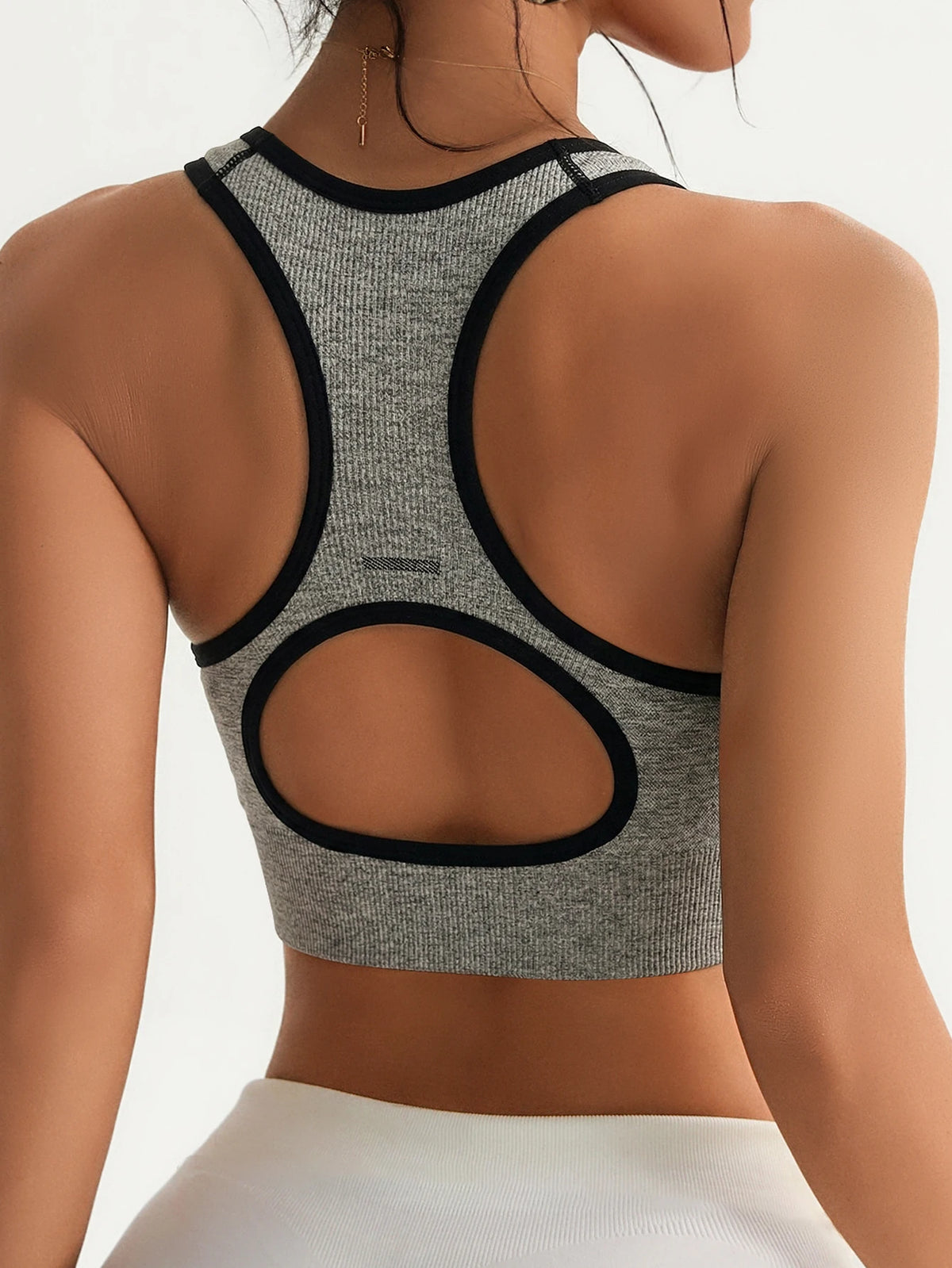 A gray seamless racerback sports bra top with black trim and a matching white bottom visible from the back.