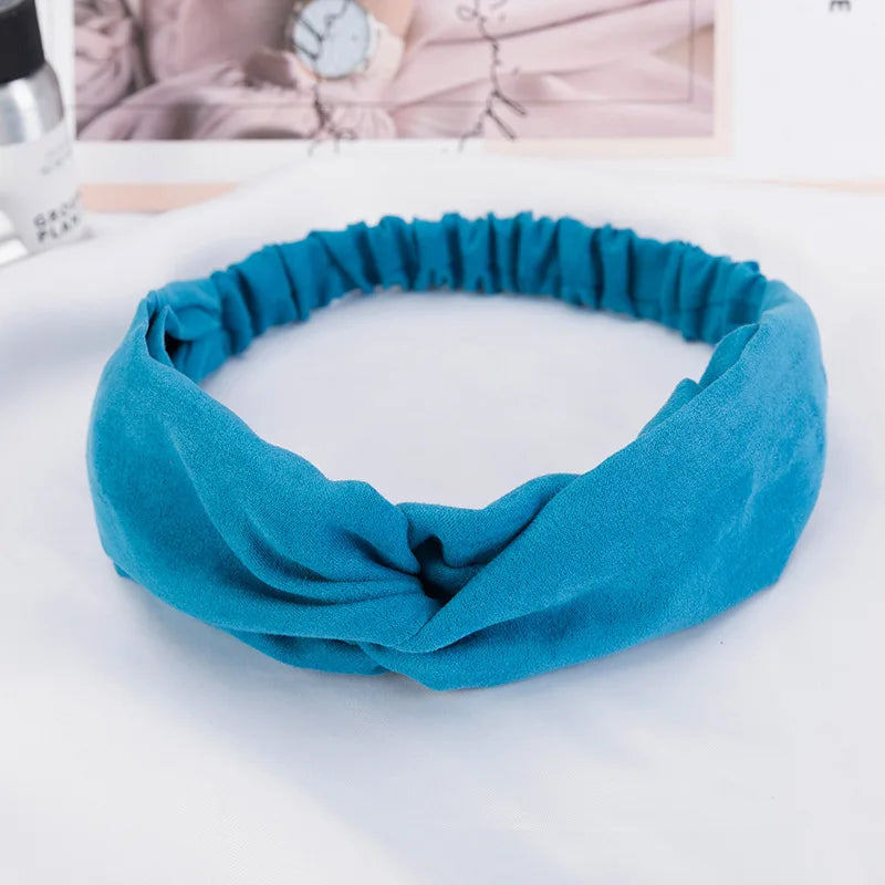 A teal fabric headband or scarf is shown laid flat on a white surface.