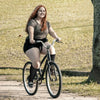 A young woman with long red hair is riding a bicycle outdoors on a dirt path.