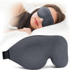A gray light blocking sleep mask is shown being worn by a woman resting on a pillow.