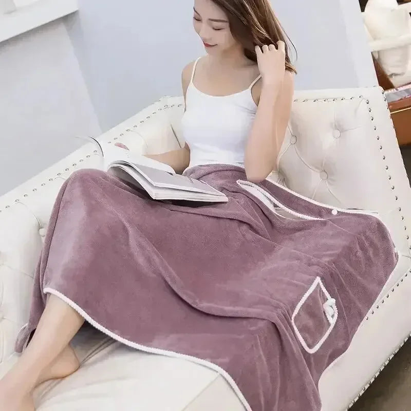 A woman wearing a mauve fleece bath robe is relaxing on a white leather sofa.