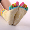 A pair of rainbow yoga socks with colorful toe tips and white polka dots on the foot.