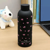 Taza térmica de acero inoxidable negra con diseños de cinta floral rosa junto a un juguete de peluche blanco.