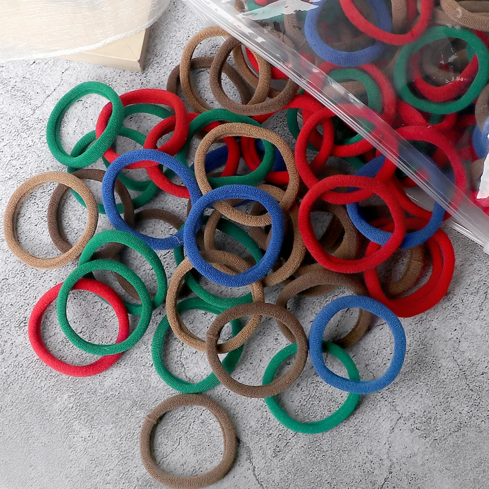 A pile of 50 pieces of mixed color elastic hair bands in red, green, blue, and brown.