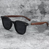 Black sunglasses with dark lenses and a brown wood grain frame resting on a gray textured surface.