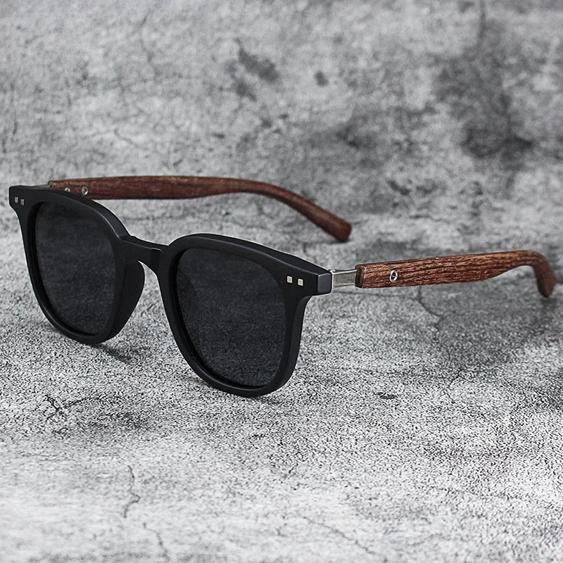 Black sunglasses with dark lenses and a brown wood grain frame resting on a gray textured surface.
