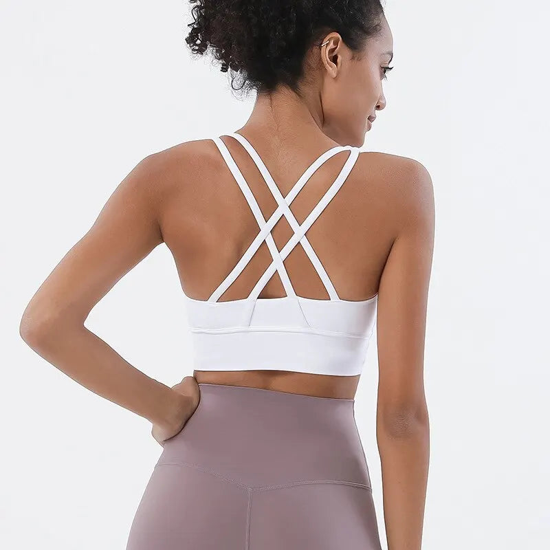 Eine Frau in einem weißen Sport-BH und mauvefarbenen Yoga-Hosen, von hinten gezeigt.
