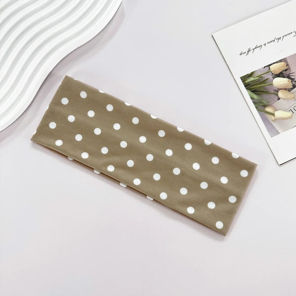 Bandeau de yoga élastique à pois beige posé sur une surface blanche à côté d'une carte imprimée de plantes.