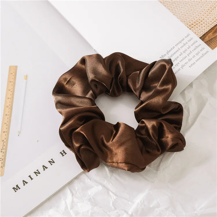 A brown satin scrunchie tied in a voluminous, ruched bow shape resting on white paper.