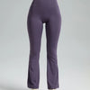 A model is wearing a purple high-waisted bootcut yoga outfit consisting of a cropped top and full-length pants.