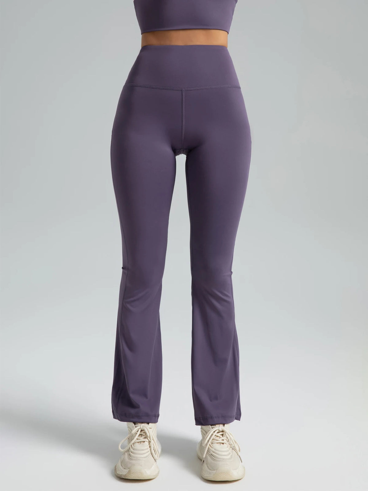 A model is wearing a purple high-waisted bootcut yoga outfit consisting of a cropped top and full-length pants.