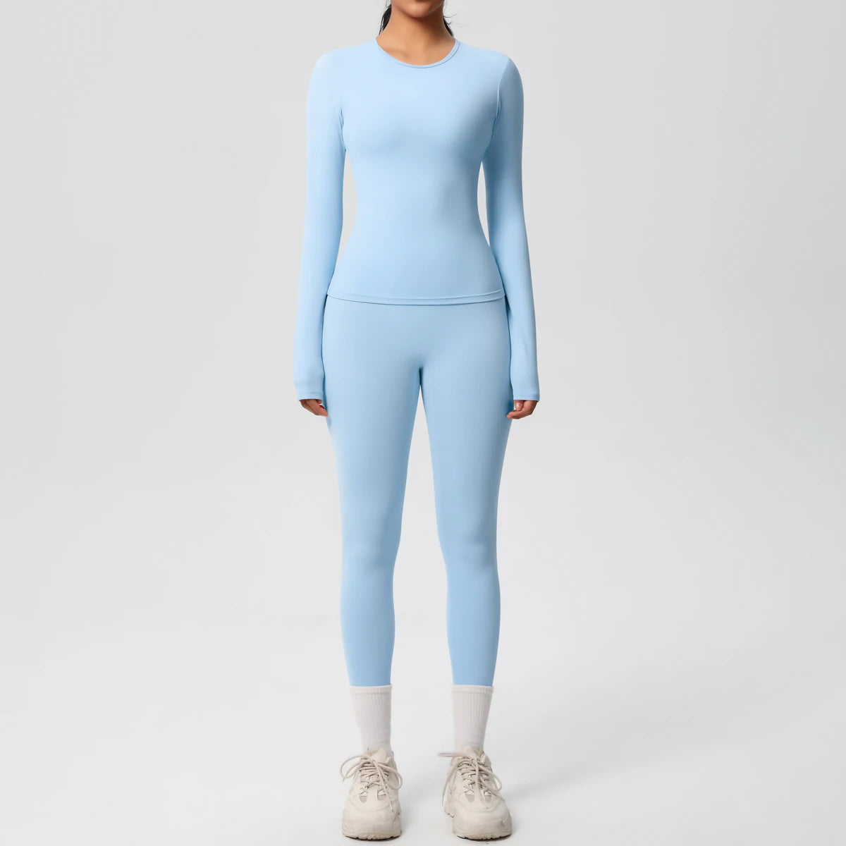 A woman wearing a light blue long-sleeved performance yoga and gym set with matching leggings and white socks.