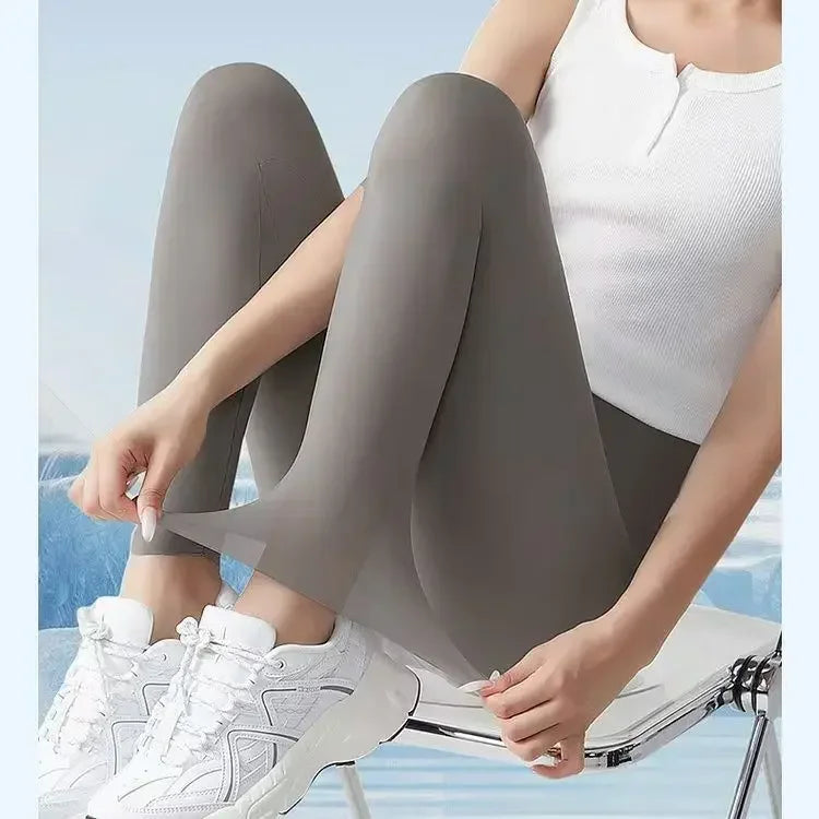 Une femme portant des leggings en peau de requin gris et un haut blanc, assise sur une surface bleu clair.