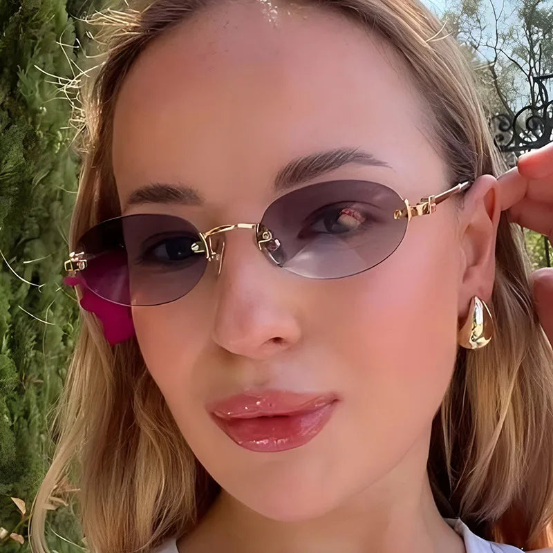 Close-up of a woman wearing rimless oval gradient sunglasses with gold accents outdoors.