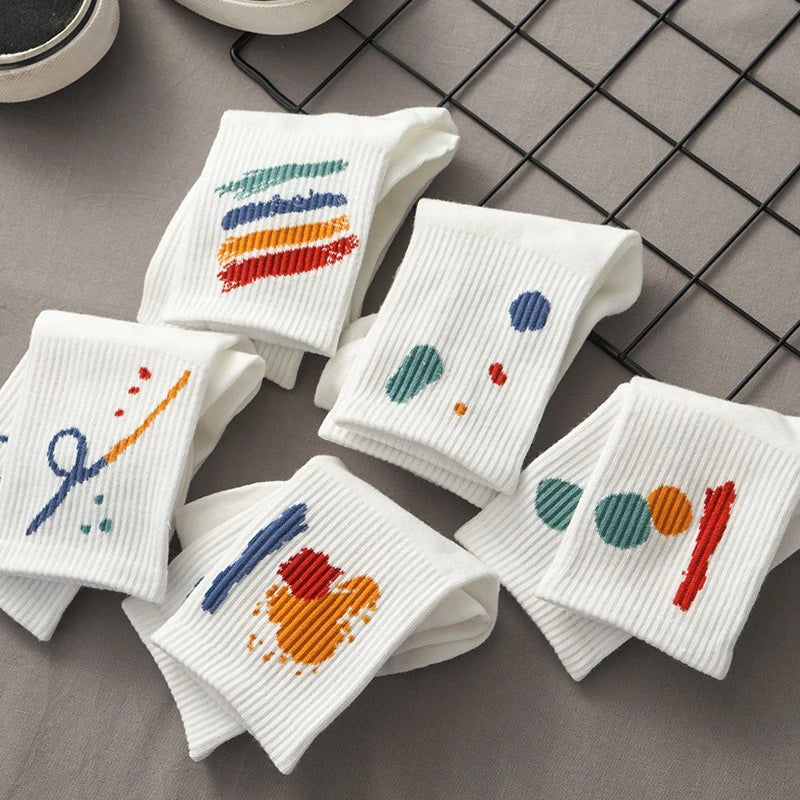 A stack of five white breathable cotton socks with colorful embroidery laid on a gray grid background.