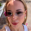 A close-up of a woman wearing rimless oval gradient sunglasses with gold accents outdoors.