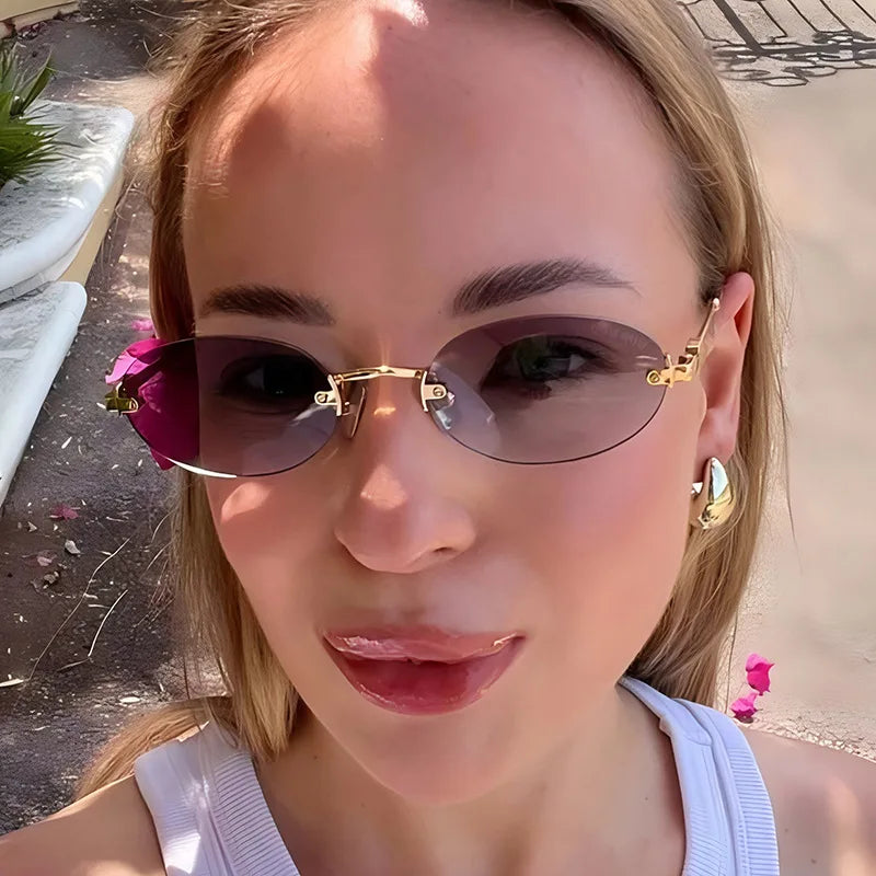 A close-up of a woman wearing rimless oval gradient sunglasses with gold accents outdoors.