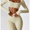 A model wearing a beige long-sleeved crop top and matching high-waisted leggings from a women's performance tracksuit set.