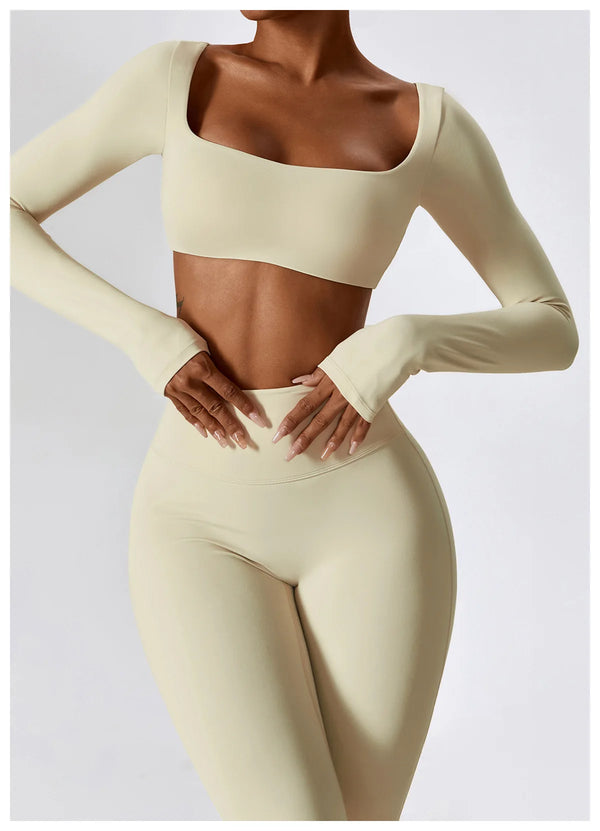 A model wearing a beige long-sleeved crop top and matching high-waisted leggings from a women's performance tracksuit set.
