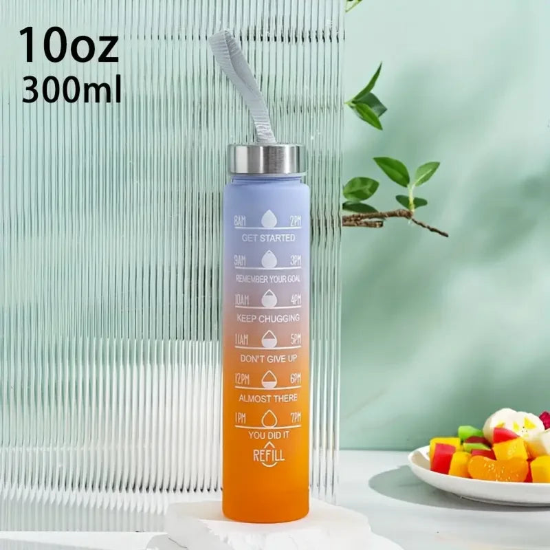 An orange water bottle with a silver straw and motivational text is shown next to a green plant.