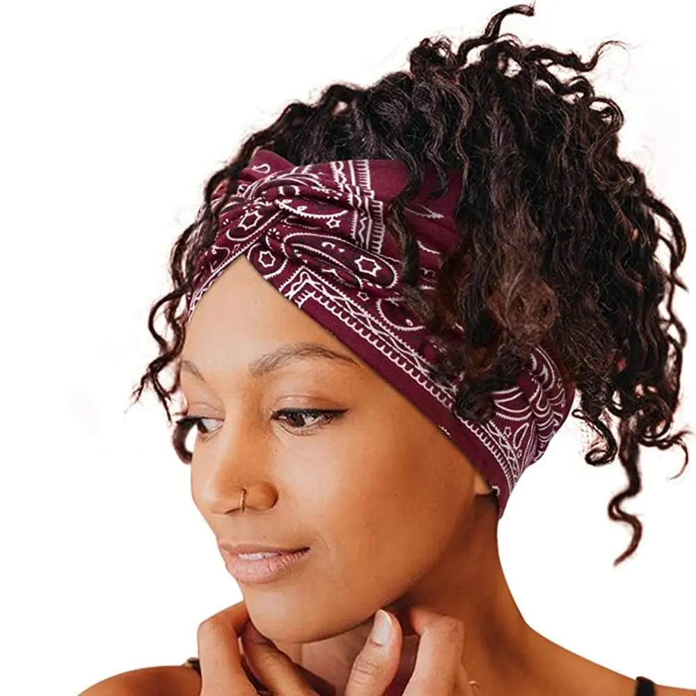 A woman with dark curly hair wears a maroon patterned fabric headband for yoga or workout.