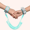 A hand is holding a turquoise adjustable child safety harness and leash, featuring silver buckles.