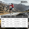 A mountain biker wearing a red jacket and helmet jumps over a wooden structure in a rugged, mountainous landscape.