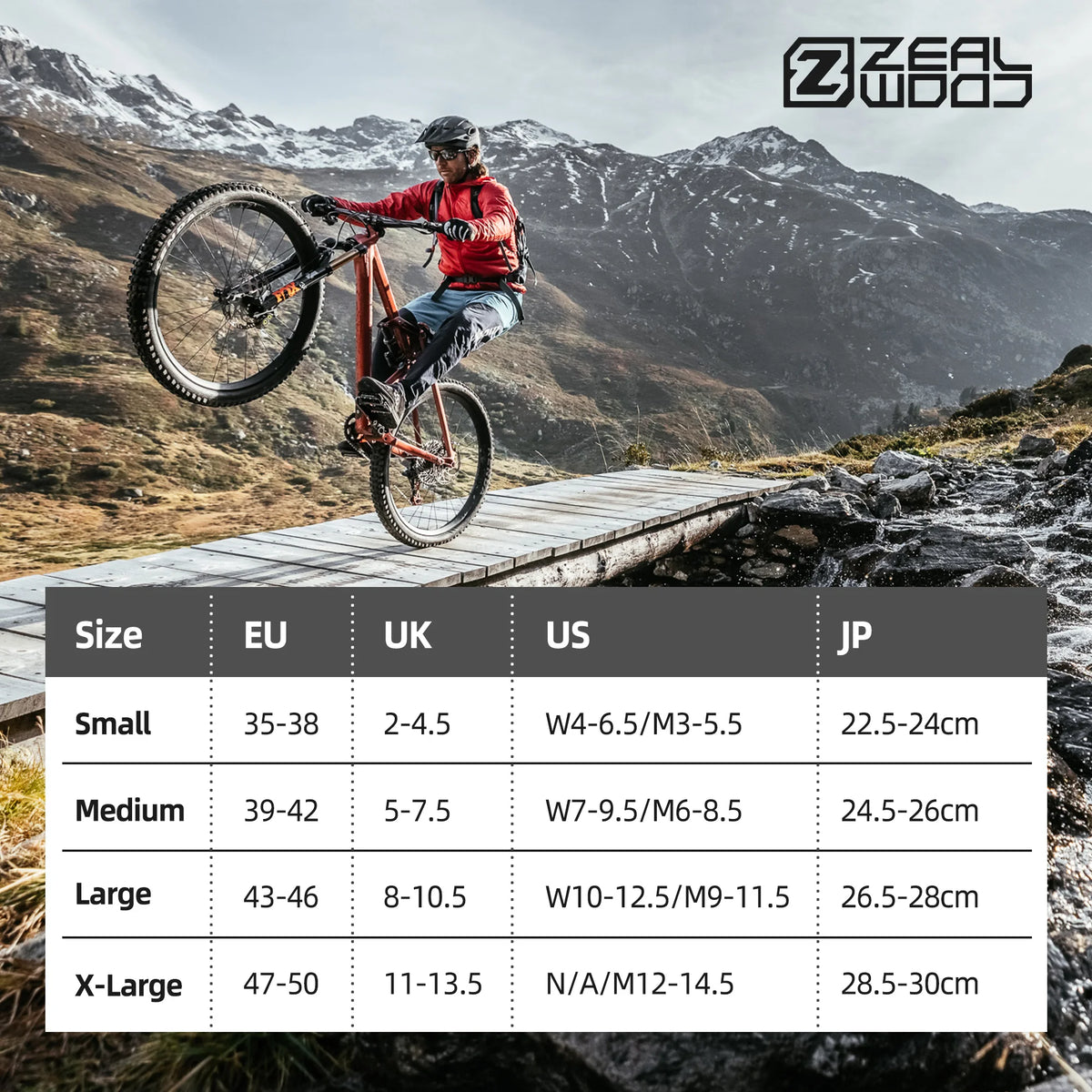 A mountain biker wearing a red jacket and helmet jumps over a wooden structure in a rugged, mountainous landscape.