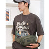 A man wearing a grey cap and brown shirt holds a olive green nylon waist bag.
