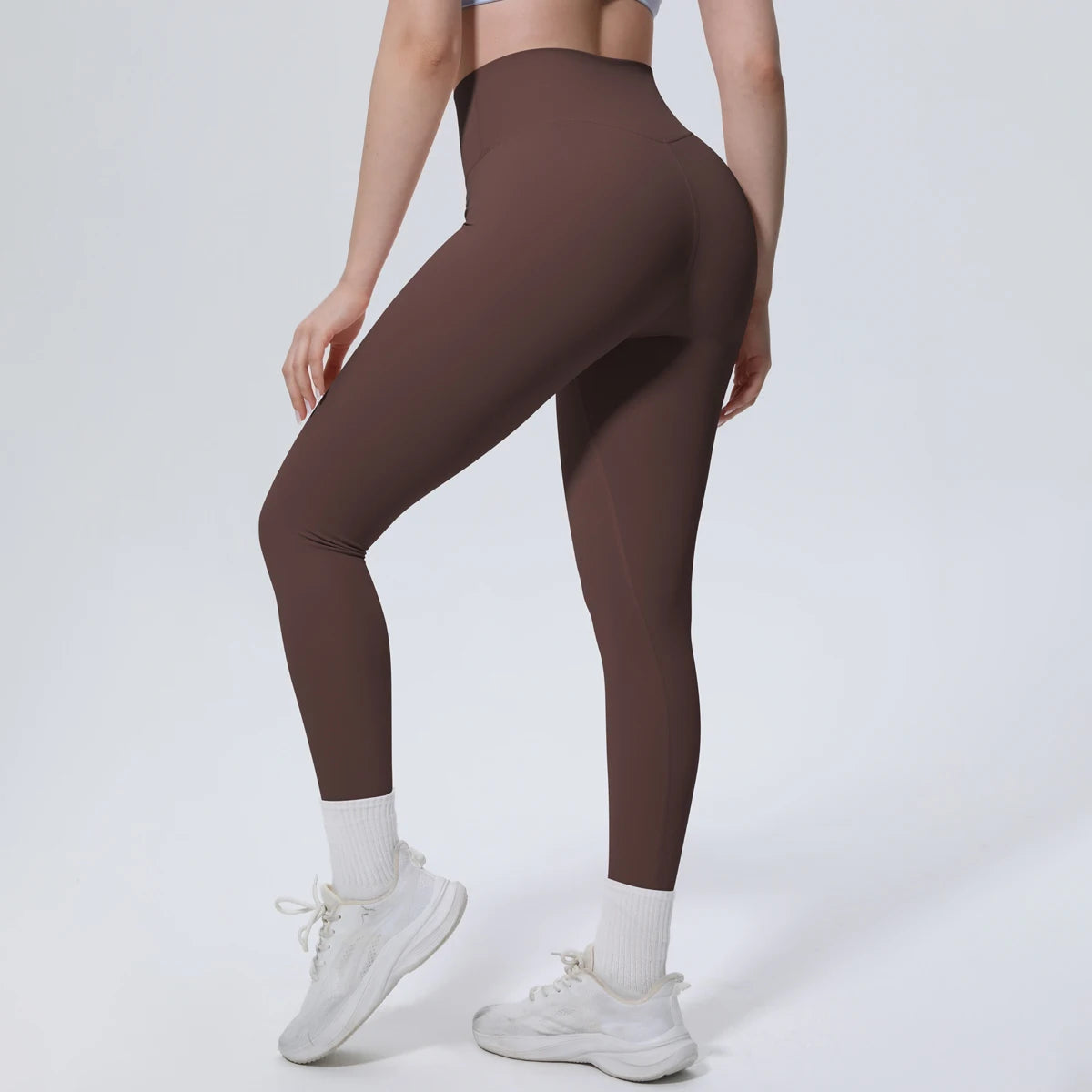 A model wearing high-waisted brown quick-drying yoga leggings and white socks, standing against a light background.
